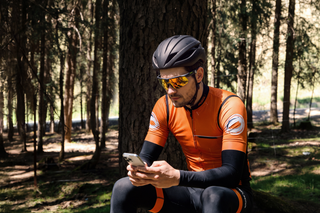 Rider sitting on a rock in the forest reviewing footage on a phone